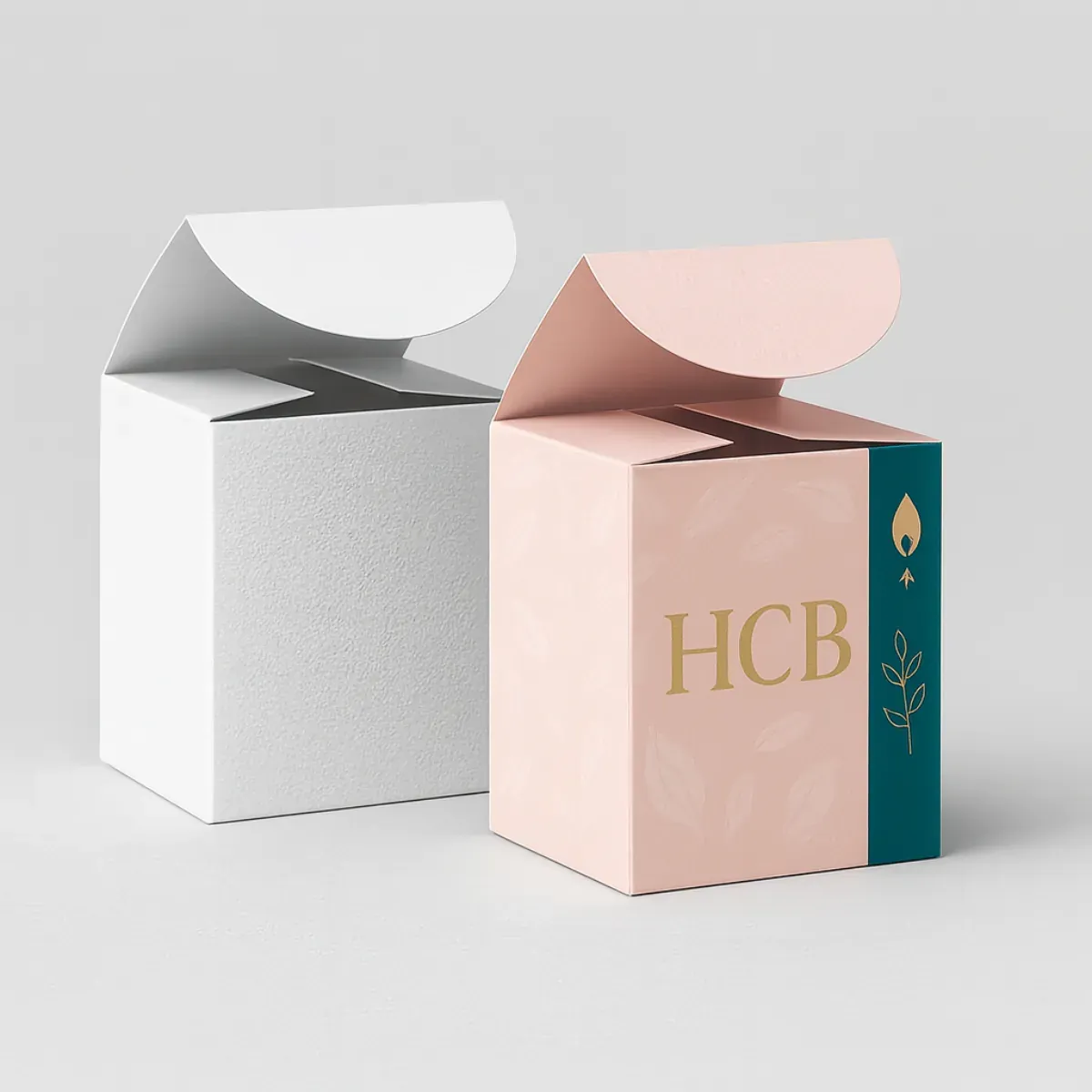 Two cube-shaped packaging boxes with round flap tops- one plain white and the other pastel pink with teal side panel- The designed box features the gold letters -HCB- with a small flame and leaf graphic-