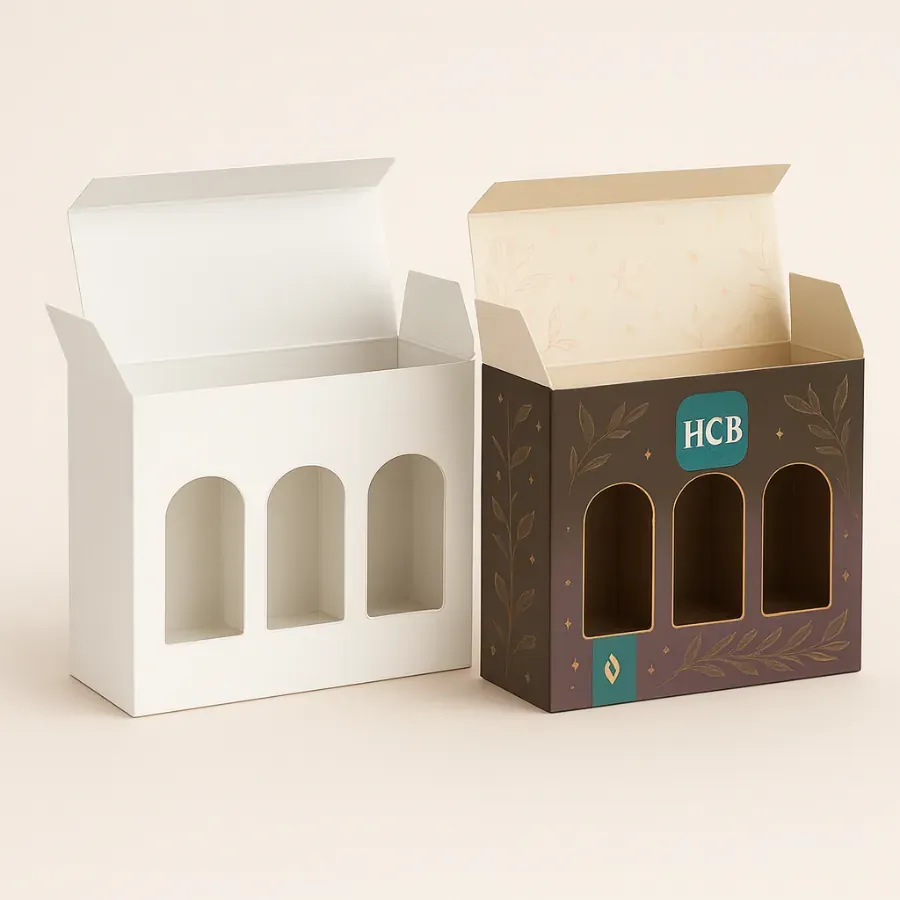 Tall candle boxes with three arched window cutouts- one plain white and one designed in dark brown with gold accents- leaves- and HCB branding class=
