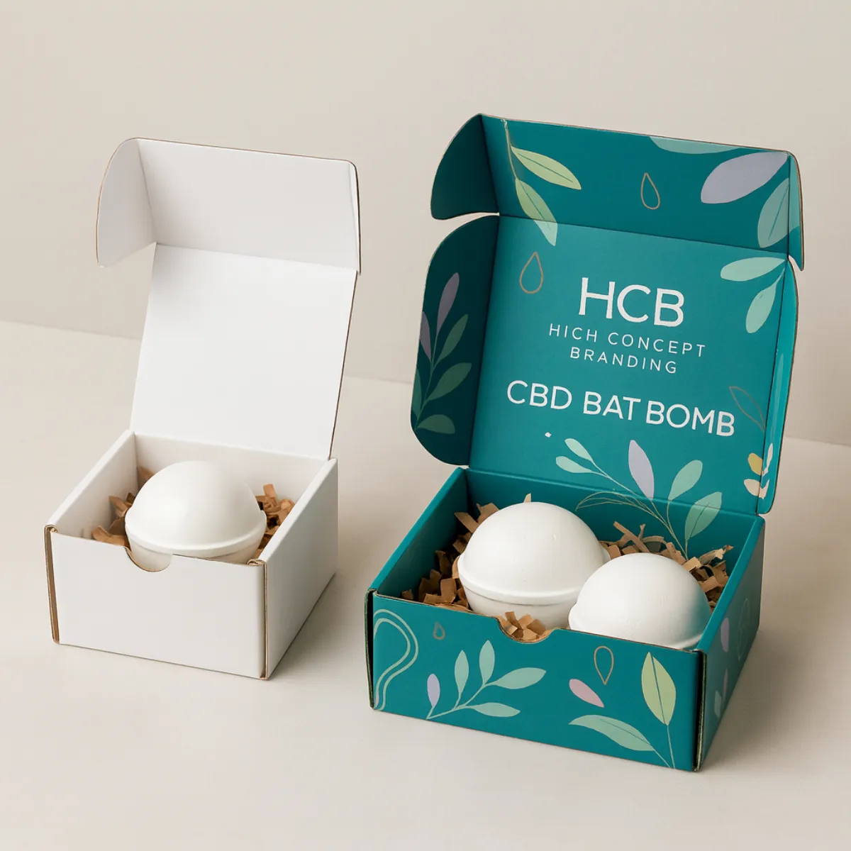 Two open rectangular boxes containing bath bombs on shredded paper- one plain white and one printed in teal and light green with -CBD BAT BOMB- text- class=
