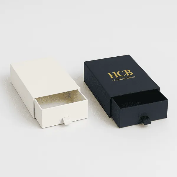 Two luxury drawer boxes with ribbon pulls one cream and one black with gold HCB branding on the lid class=