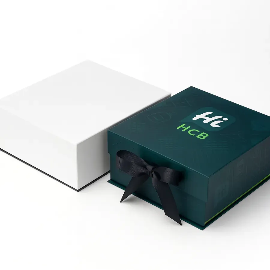 ustom collapsible magnetic box wrapped with a black satin bow- A plain white box is positioned next to a dark teal box with a custom logo print on the lid class=