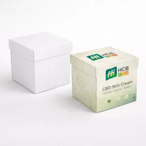 Two square cardboard boxes, one plain white and one featuring green botanical branding for CBD cream.