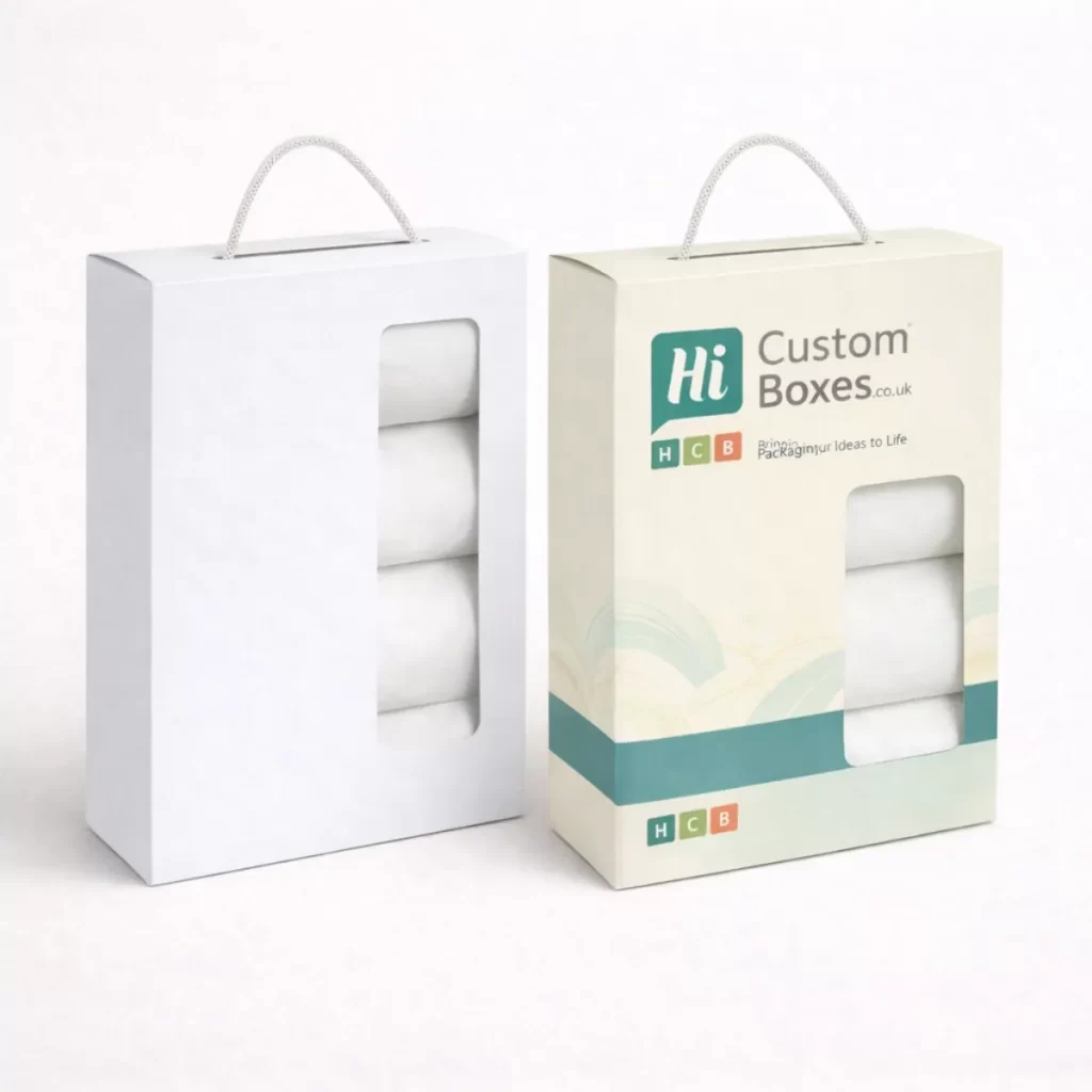 Two vertical retail boxes with rope handles and transparent windows showing folded white linen.