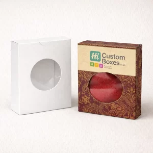 Two upright retail boxes with circular window cut-outs, showing a red shawl through the branded version.