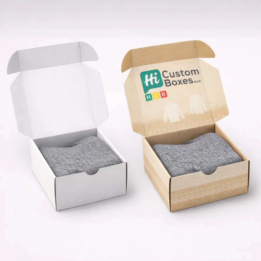 Two open mailer boxes, one white and one branded kraft, containing neatly folded grey knitwear.