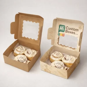 Two small square pastry boxes with scalloped window lids, displaying four generously frosted cinnamon rolls in each.
