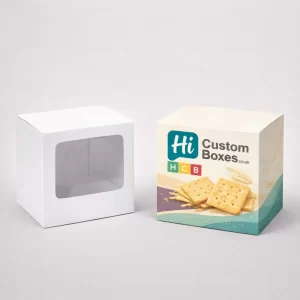 Square cracker packaging with a clear front window next to a printed branded box.