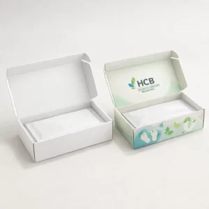 Two small white cardboard boxes, one plain and one with green branding, containing sealed sachets.