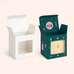 Two candle packaging boxes- one plain white with a front window cutout- and the other fully printed in dark teal with pink- yellow- and green candle-themed illustrations and HCB branding