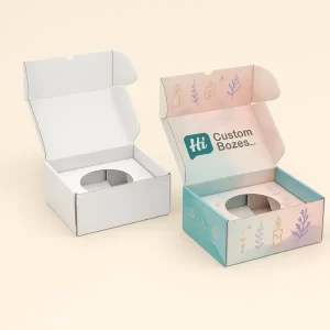 Two open custom tuck-top boxes with inserts, one plain white and one pastel-printed with branding and candle-themed illustrations.