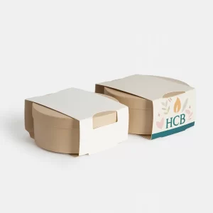 Round candle boxes with top sleeves, one plain white and the other featuring HCB logo with decorative pastel floral accents.