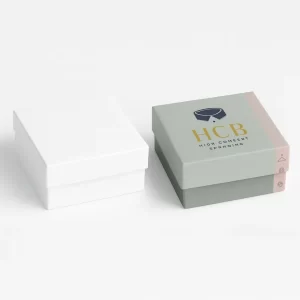 Two square rigid apparel boxes with lids- one plain white and the other in green with pink side band- featuring -HCB- logo and collar icon design