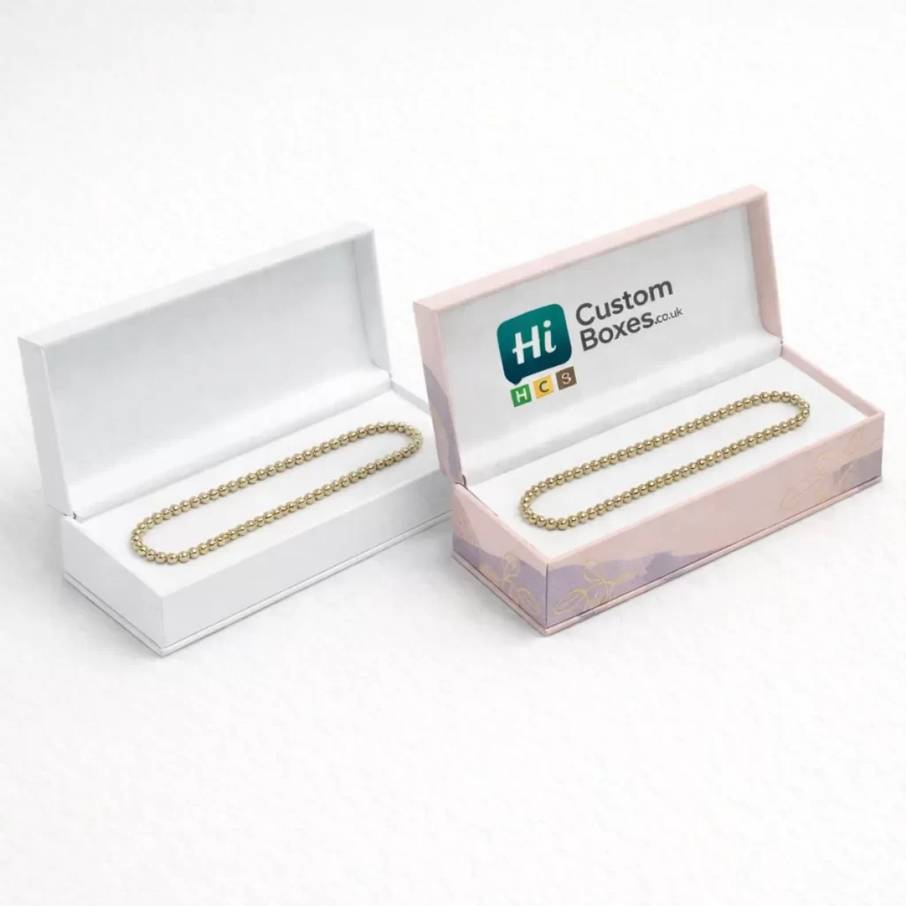 Elegant white and pink hinged boxes displaying gold beaded anklets on soft white padded inserts