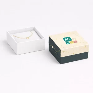 A plain white jewellery box next to a branded cream and navy box featuring a gold bracelet