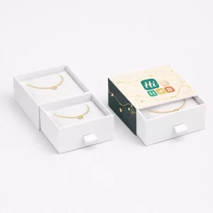 Two white drawer-style jewellery boxes- one partially pulled open to reveal a gold bracelet on a cushion