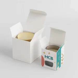 Two white 50cl candle boxes, one open with a candle and one printed with an HCB logo.